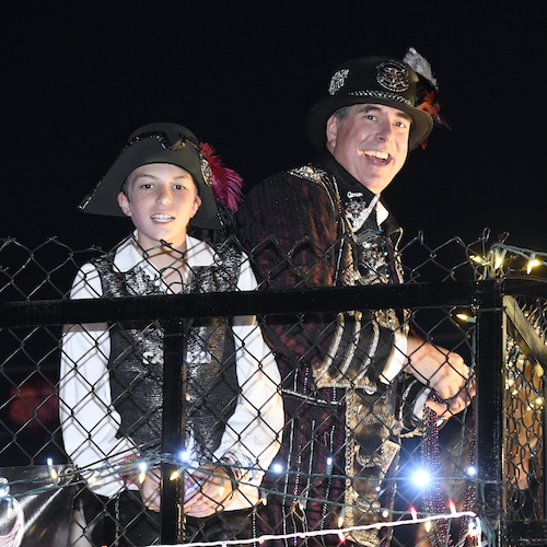 Man dressed as a pirate captain and a boy dressed as a pirate, both smiling on a float